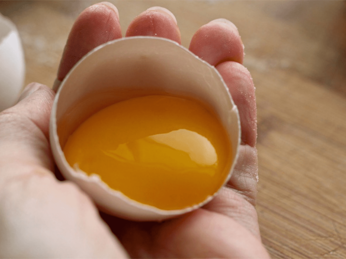 Person hand holding a cracked egg with yolk showing.