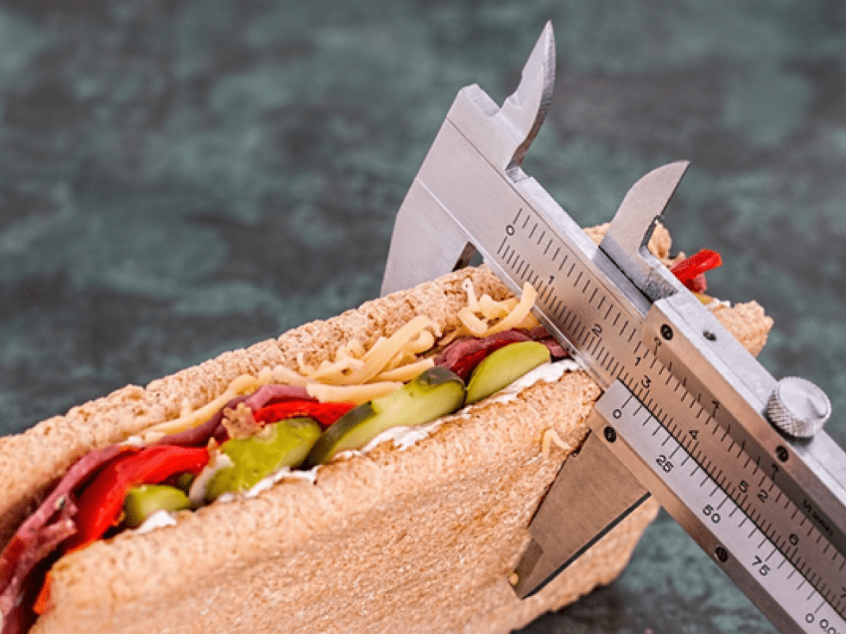 Sandwich bread with cucumber, capsicum and cheese with a ruler wrapped around it.